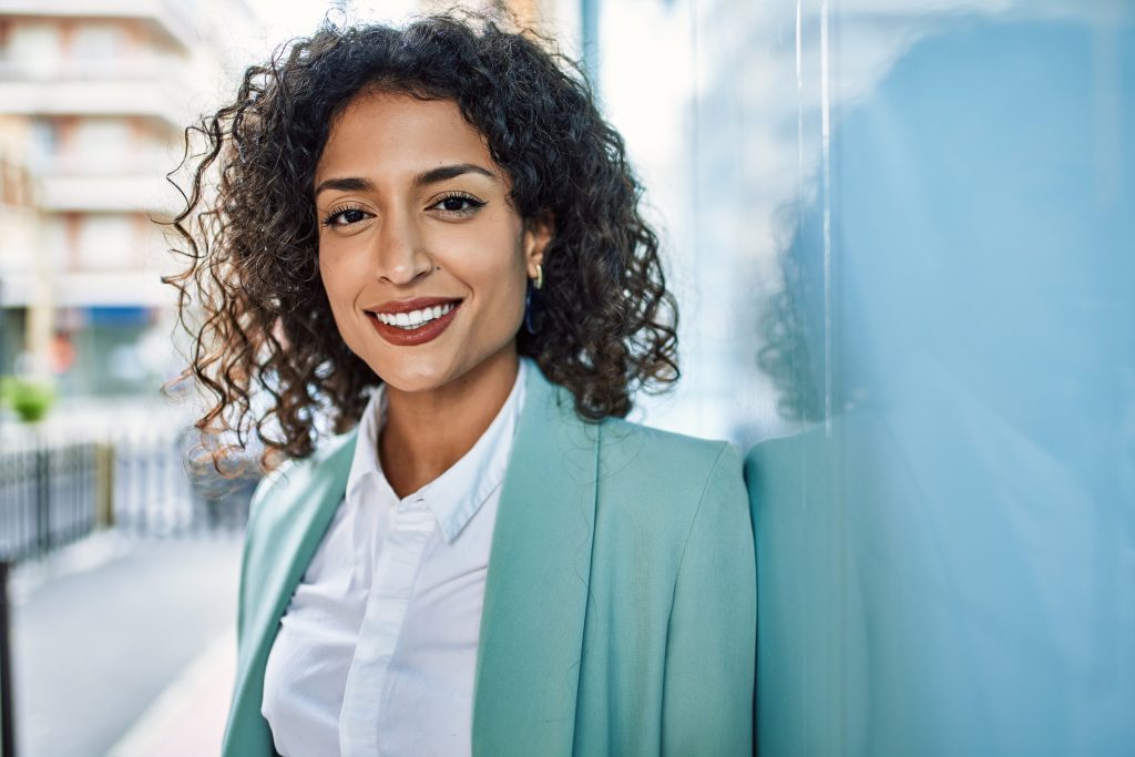 Young business woman wearing professional look smiling confident at the city leaning on the wall.